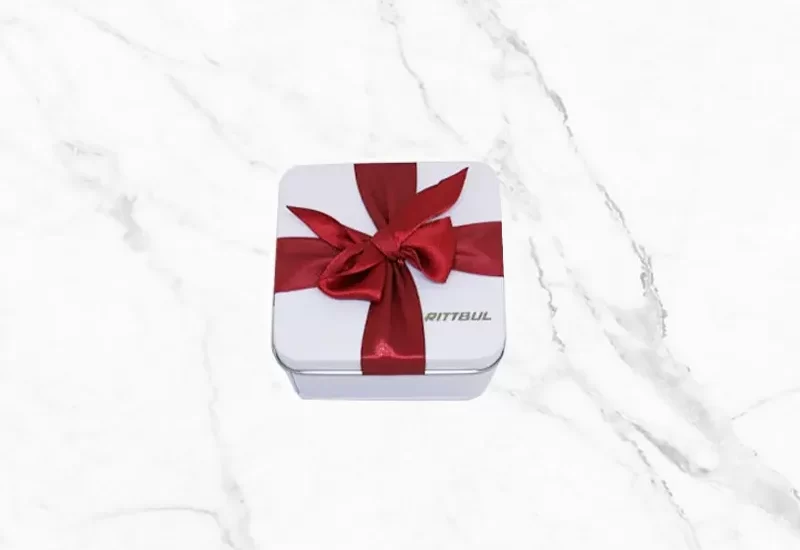 Red Ribbon Easter – бяла метална великденска кутия с червена панделка и шоколадови яйца.